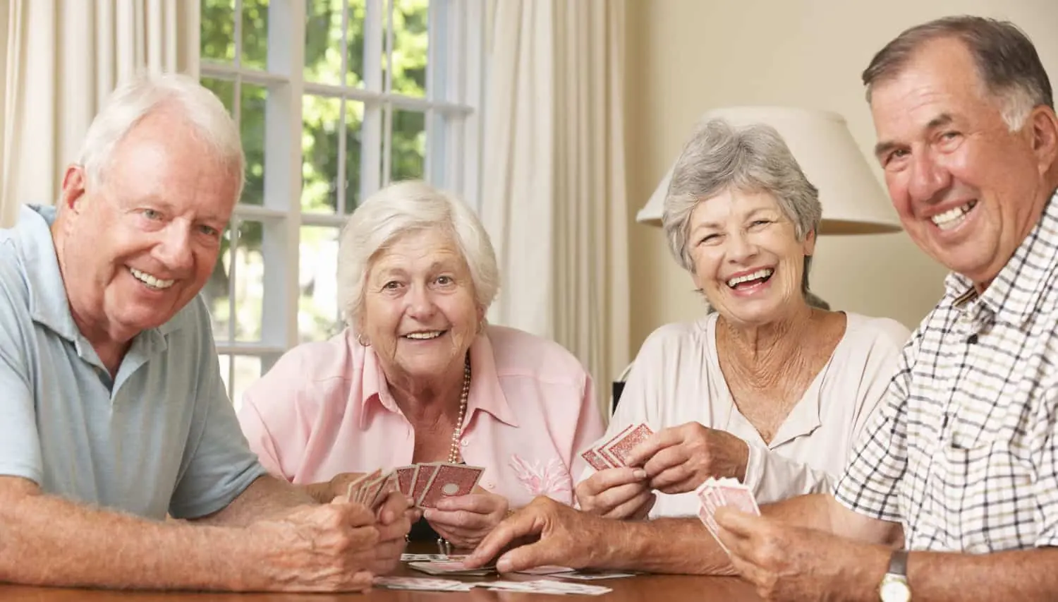 Four senior friends laughing over a game of cards