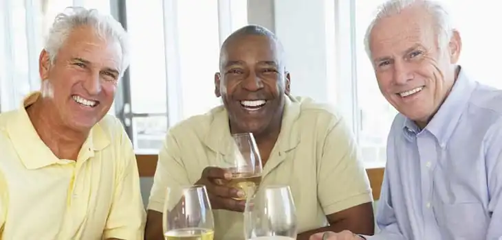 Three senior men laughing together over glasses of white wine