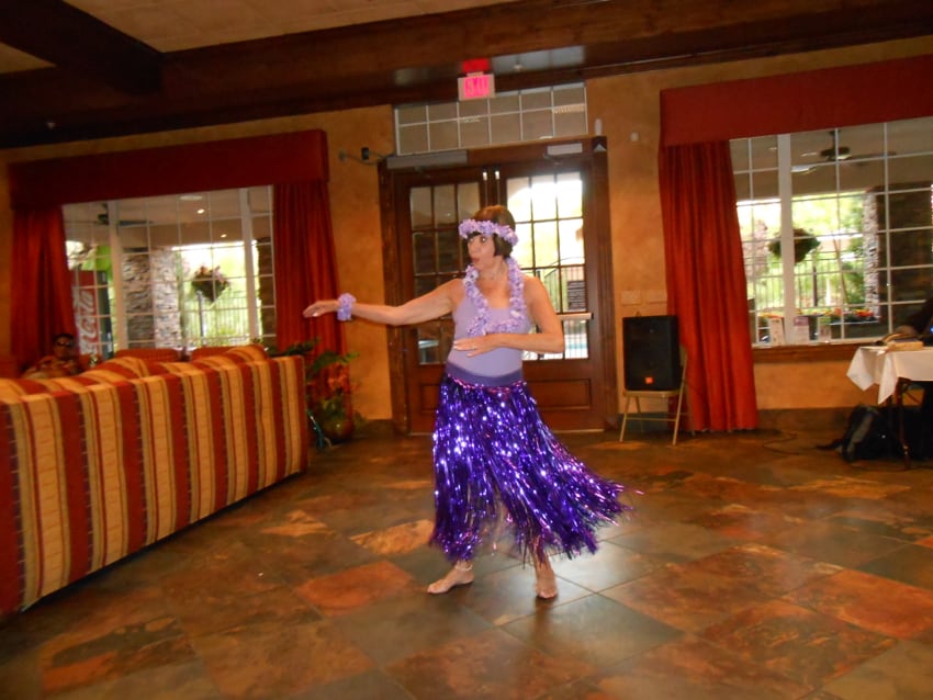 Resident in a purple hula skirt dancing at a luau party in the Carefree clubhouse