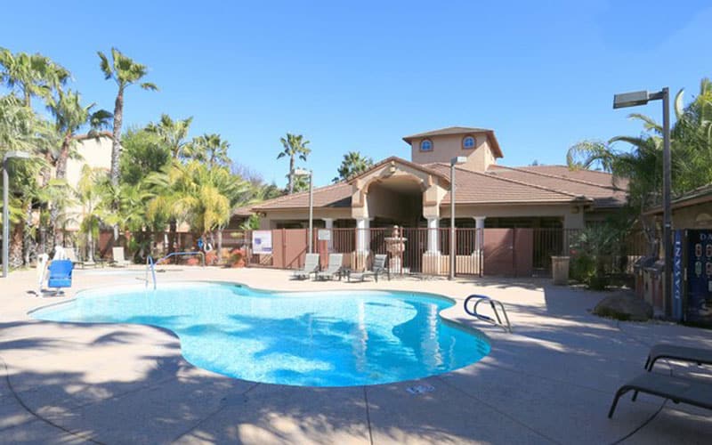 Kidney-shaped outdoor pool and clubhouse surrounded by palm trees at Carefree Senior Living