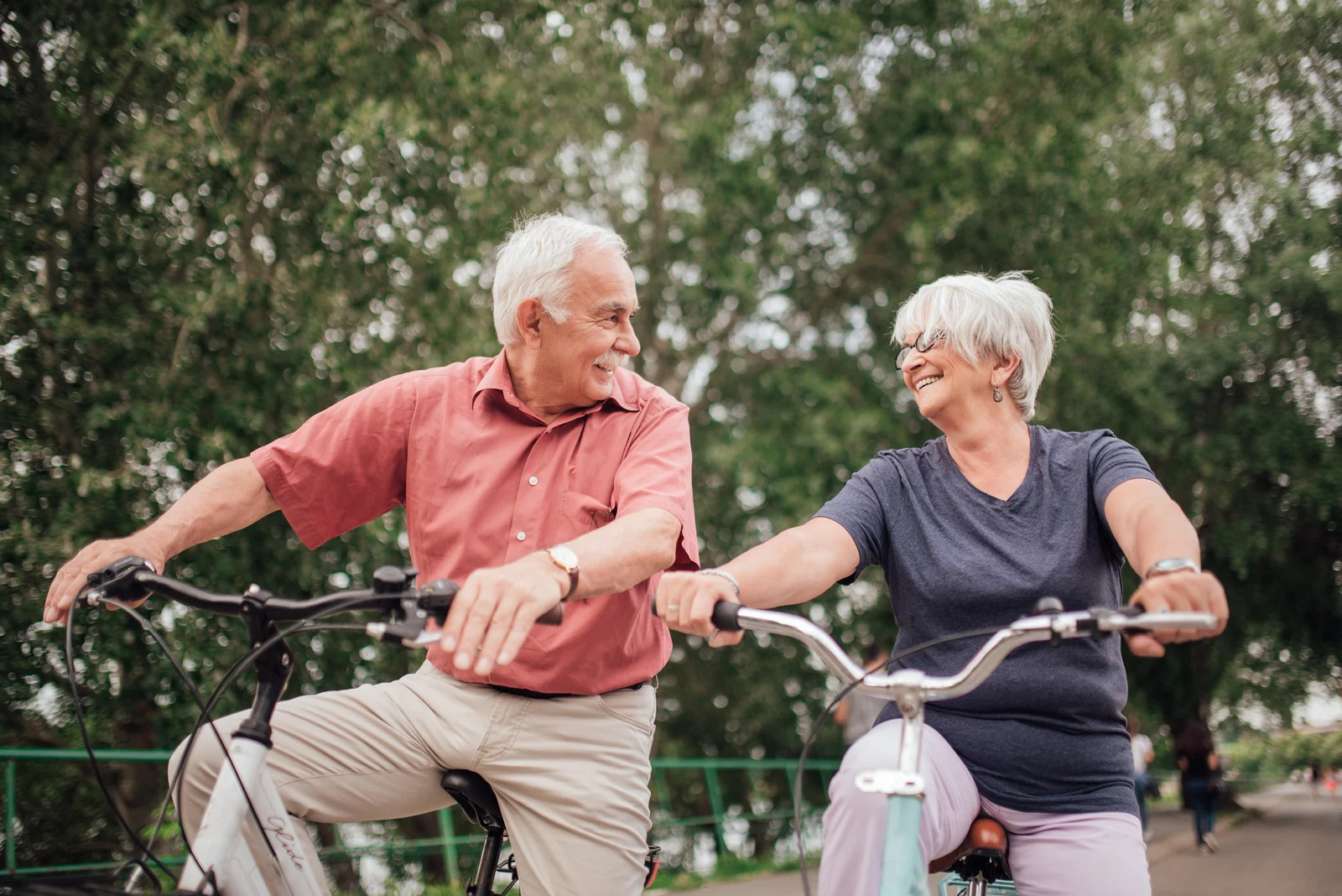 Older couple smiling while cycling in a park